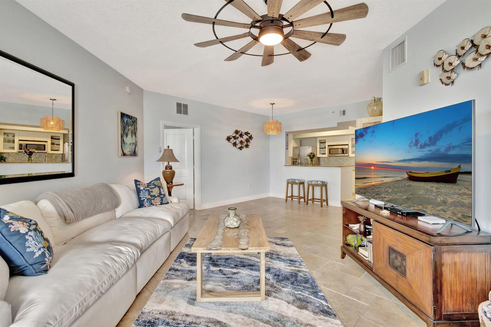 A living room features a white sofa, a wooden coffee table, and a large television — 975 NW Flagler Avenue # 407, Stuart FL 34994, STUART, FL