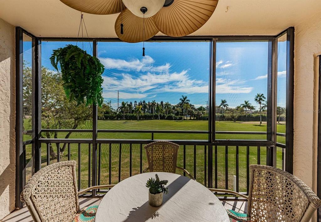 A screened-in balcony with wicker furniture overlooks a green golf course under a blue sky — 5724 PUERTA DEL SOL BOULEVARD S UNIT 248, ST PETERSBURG, FL