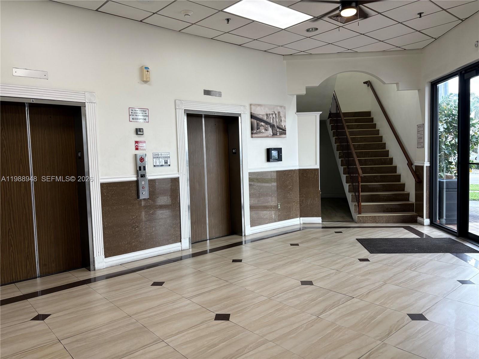 A building lobby features two elevators, a staircase, tiled floors, and brown wainscoting — 2100 W 76th St # 206, Hialeah FL 33016, HIALEAH, FL
