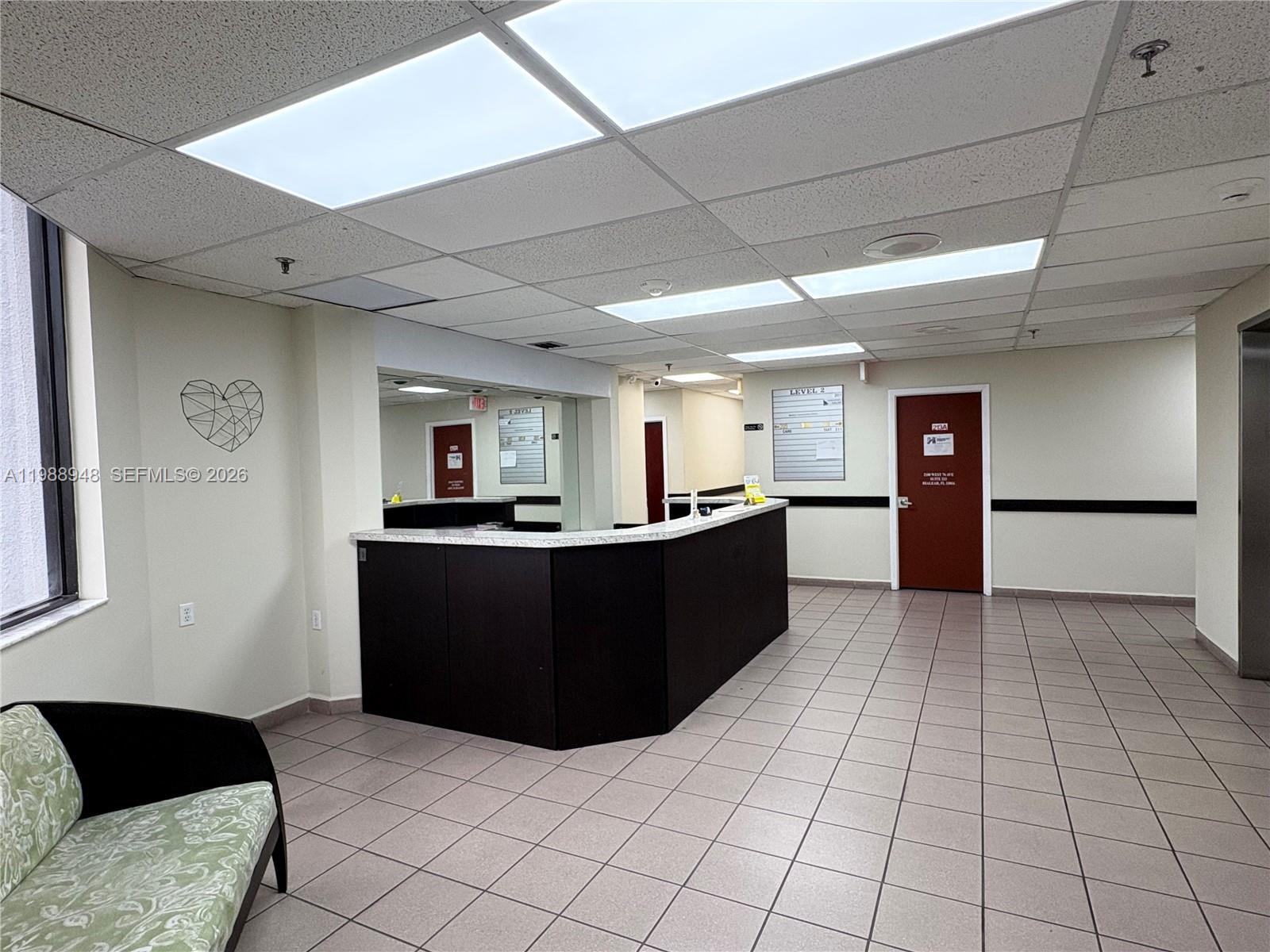 A reception area features a dark desk, tiled floors, drop ceiling, and a red door — 2100 W 76th St # 206, Hialeah FL 33016, HIALEAH, FL
