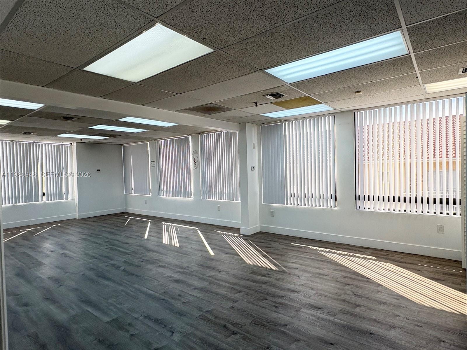An empty office space features gray wood-look flooring, white walls, and vertical window blinds — 2100 W 76th St # 206, Hialeah FL 33016, HIALEAH, FL