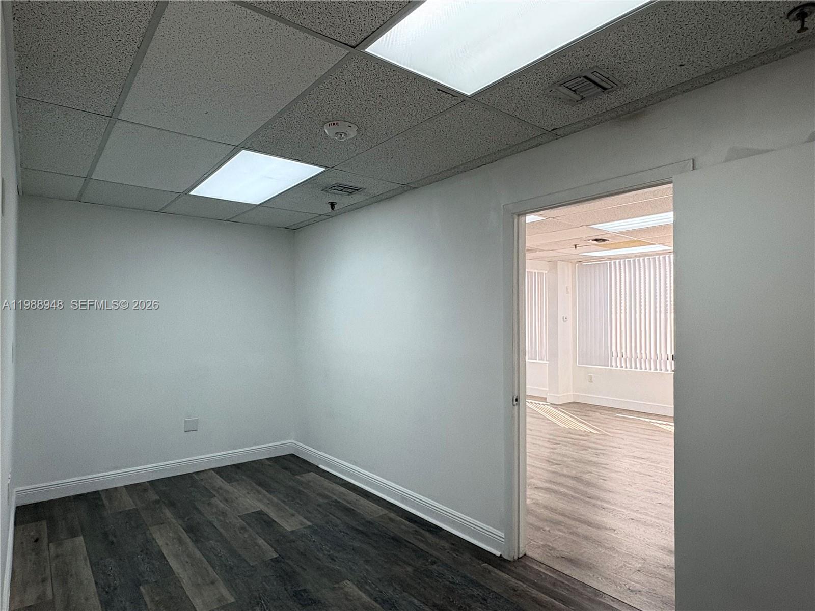 An empty office room features white walls, dark wood-look flooring, and a drop ceiling — 2100 W 76th St # 206, Hialeah FL 33016, HIALEAH, FL