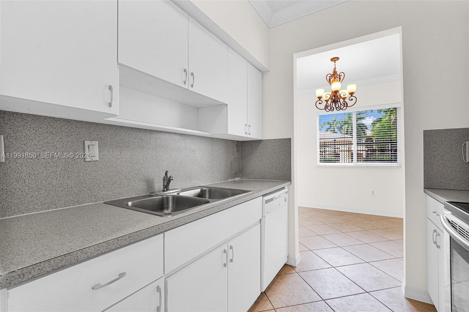 A kitchen with white cabinets, gray countertops, and a stainless steel sink leads to a dining area — 7085 Nova Dr # 128, Davie FL 33317, DAVIE, FL