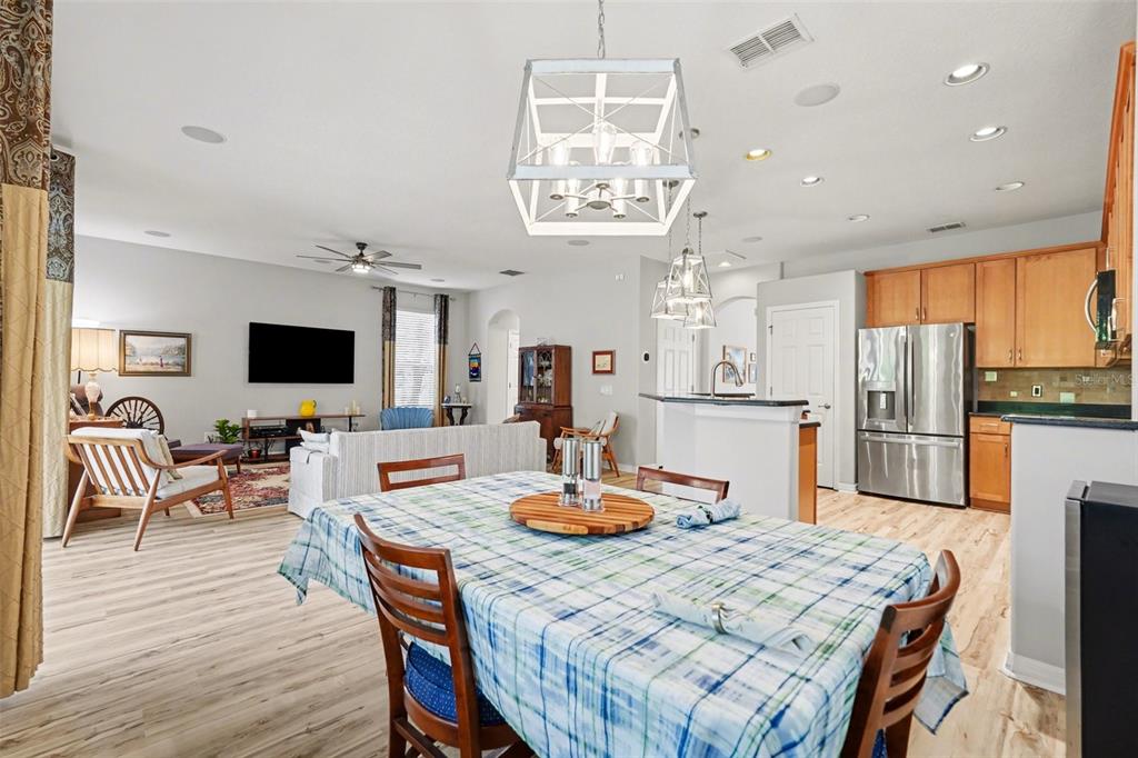 An open-concept living and dining area features light wood flooring, a plaid tablecloth, and cabinetry — 11201 GREEN PARK CIRCLE, TAMPA, FL