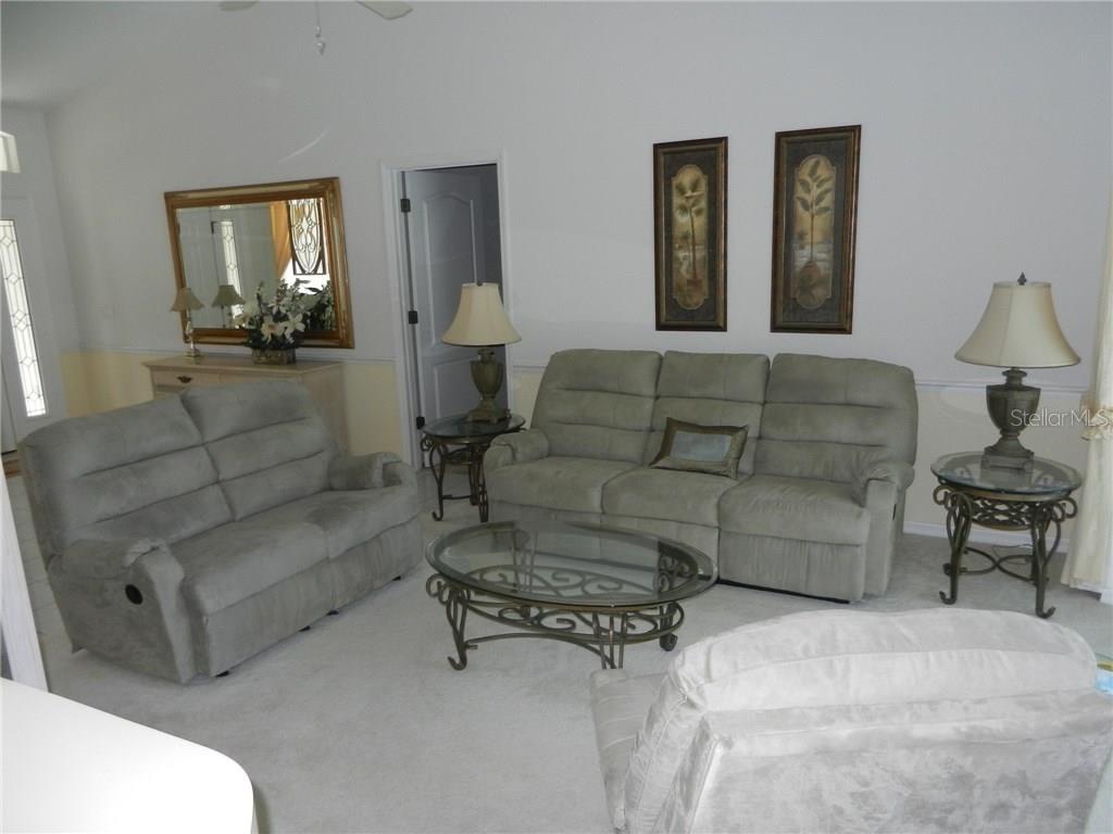 A living room features light-colored carpet, a sofa, a loveseat, and glass-topped tables — 589 ROTONDA CIRCLE, ROTONDA WEST, FL