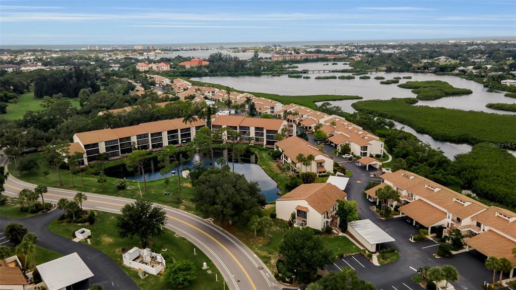 An aerial view shows a multi-building residential complex surrounded by greenery, water, and parking areas — 1142 BIRD BAY WAY UNIT 301, VENICE, FL