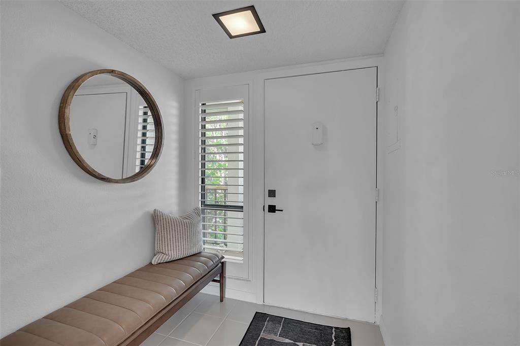 An entryway features a brown leather bench, a round mirror, and a white door — 1142 BIRD BAY WAY UNIT 301, VENICE, FL