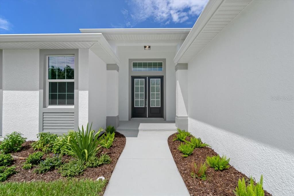 A concrete walkway leads to the double front doors of a white stucco house — 6999 BURNSVILLE STREET, ENGLEWOOD, FL