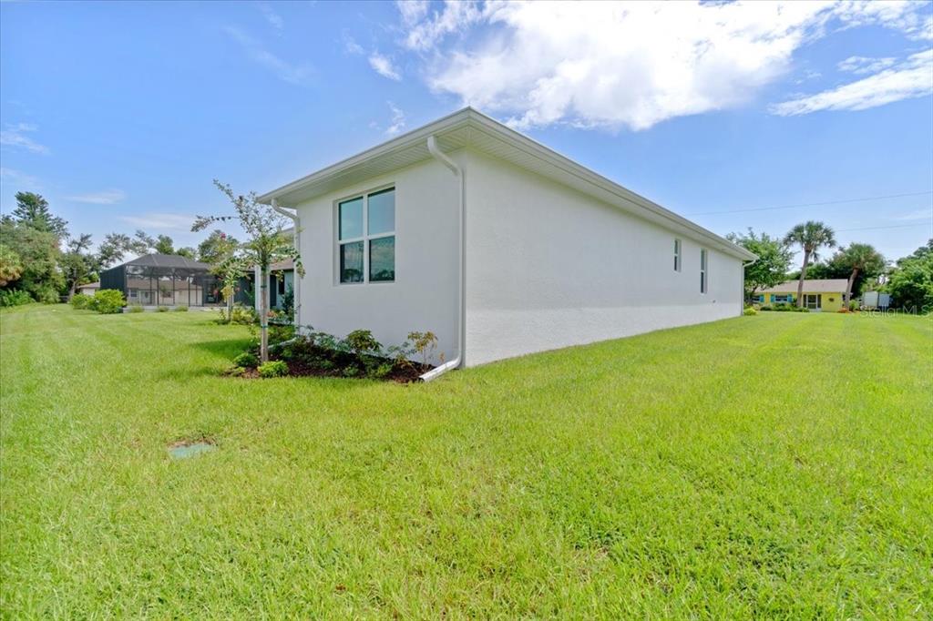 The exterior side view of a white house features a single window and green lawn — 6999 BURNSVILLE STREET, ENGLEWOOD, FL