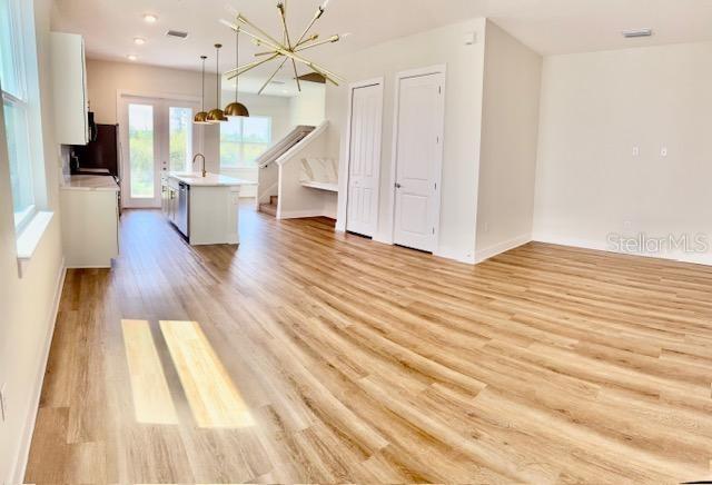 An open-concept kitchen and living area features light wood-look flooring and a modern gold chandelier — 1612 BIRCHFIELD COVE, OVIEDO, FL
