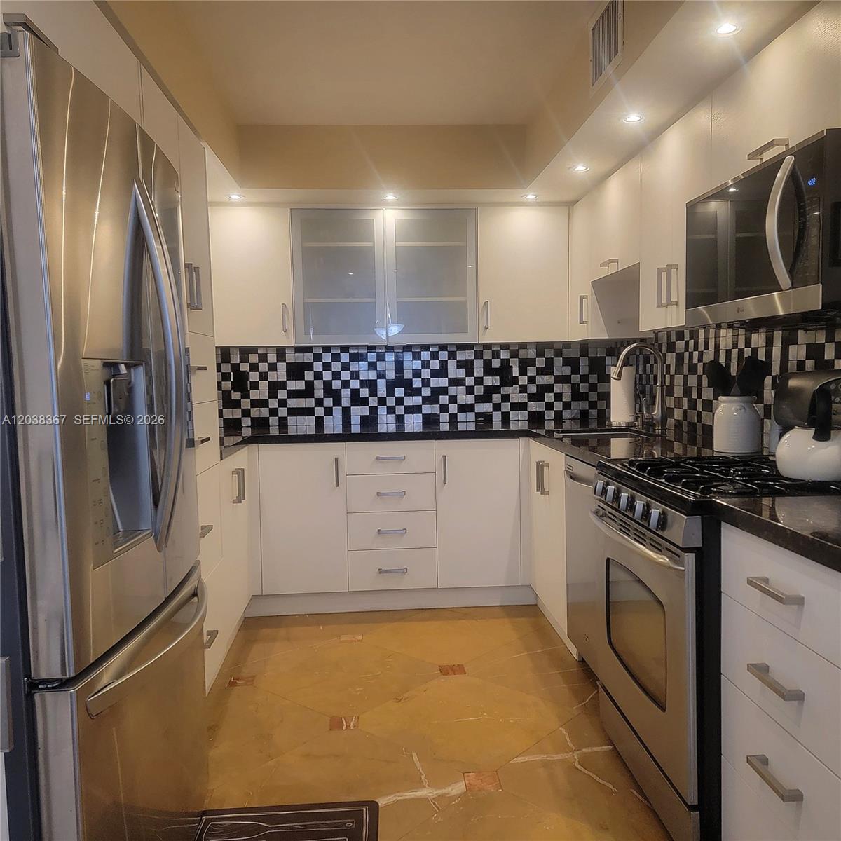 A galley kitchen features white cabinets, stainless steel appliances, and a black-and-white checkered tile backsplash — 2030 S Ocean Dr # 1718, Hallandale Beach FL 33009, HALLANDALE BEACH, FL
