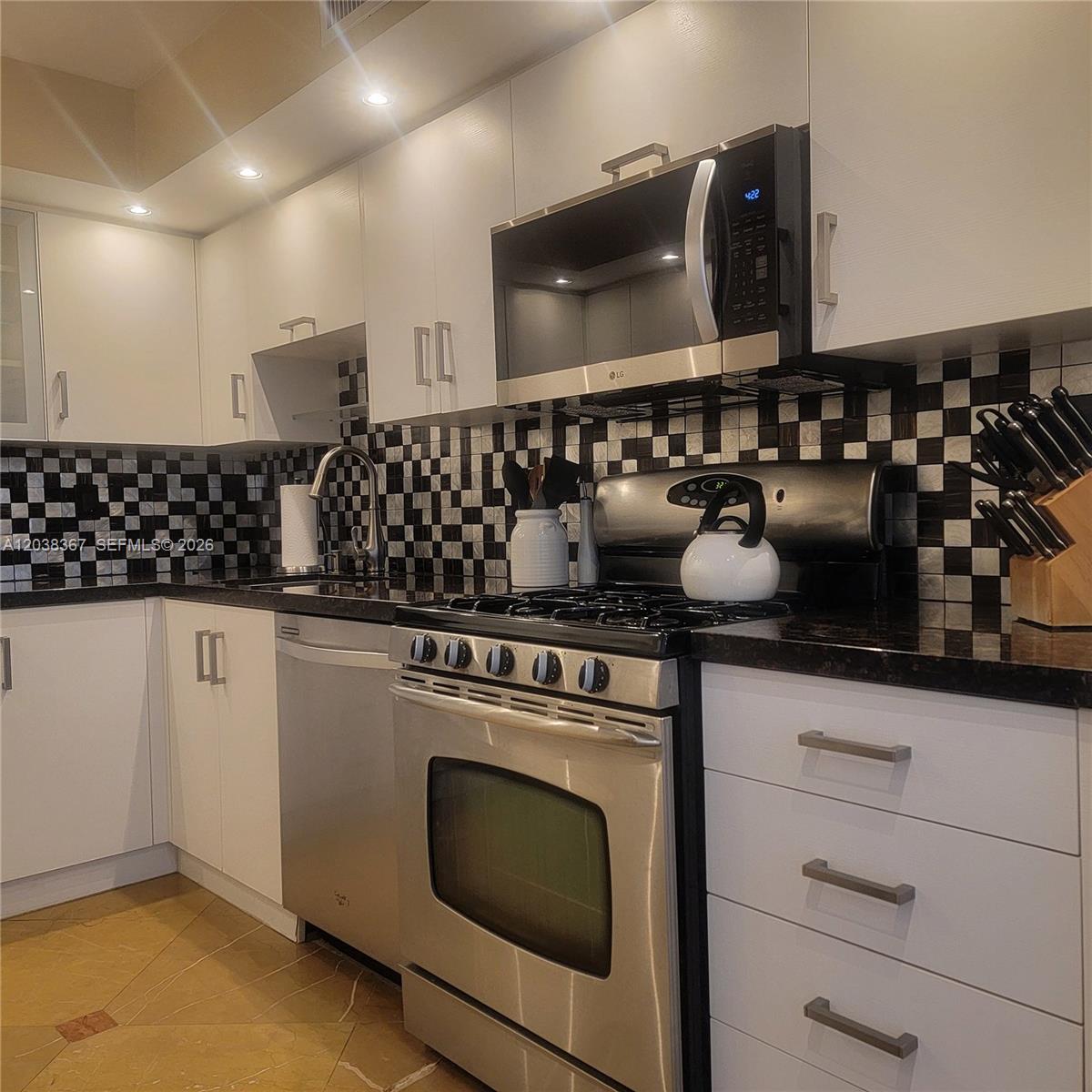 A kitchen features white cabinets, stainless steel appliances, and a black and white checkered backsplash — 2030 S Ocean Dr # 1718, Hallandale Beach FL 33009, HALLANDALE BEACH, FL