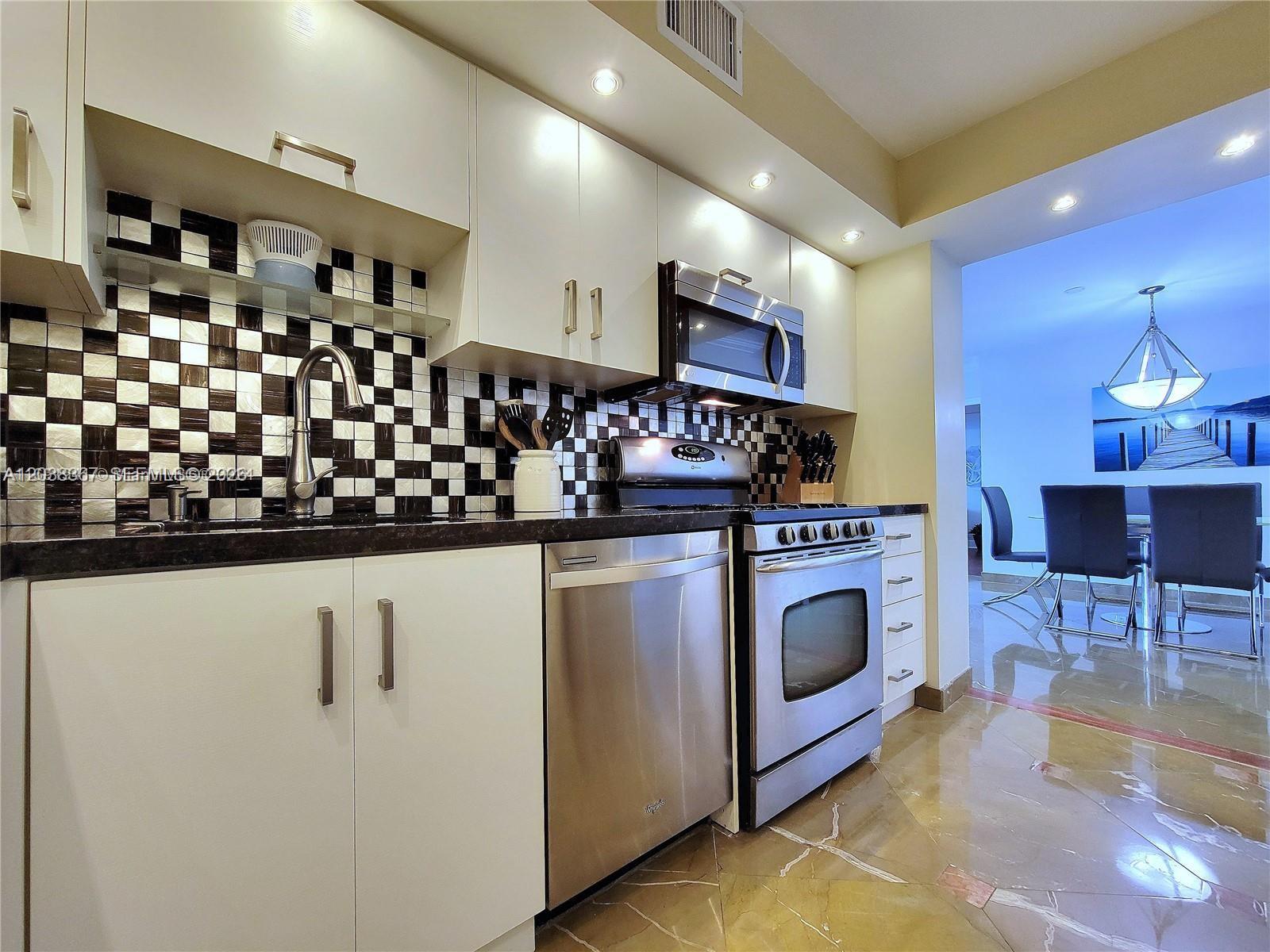 A kitchen features white cabinets, stainless steel appliances, and a black-and-white checkered tile backsplash — 2030 S Ocean Dr # 1718, Hallandale Beach FL 33009, HALLANDALE BEACH, FL