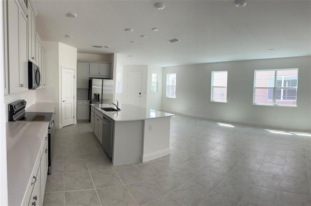 A kitchen with white cabinets and a center island opens into a spacious living area — 4806 PRAIRIE PRESERVE RUN, ST CLOUD, FL