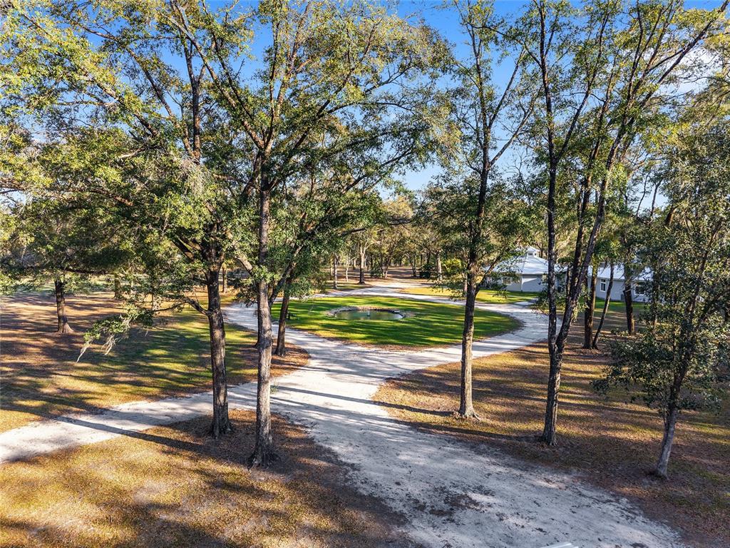 An aerial view shows a circular dirt driveway surrounding a small pond among many trees — 6012 NW 168TH STREET, ALACHUA, FL