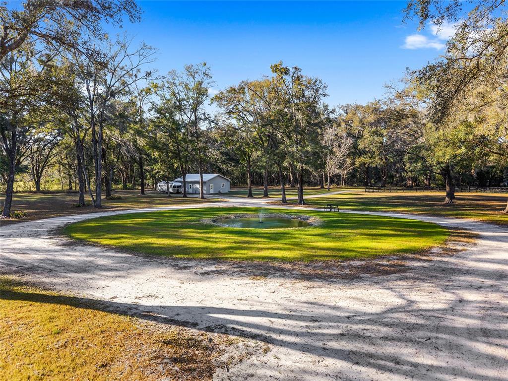 A circular driveway surrounds a small pond with a fountain in a wooded yard — 6012 NW 168TH STREET, ALACHUA, FL