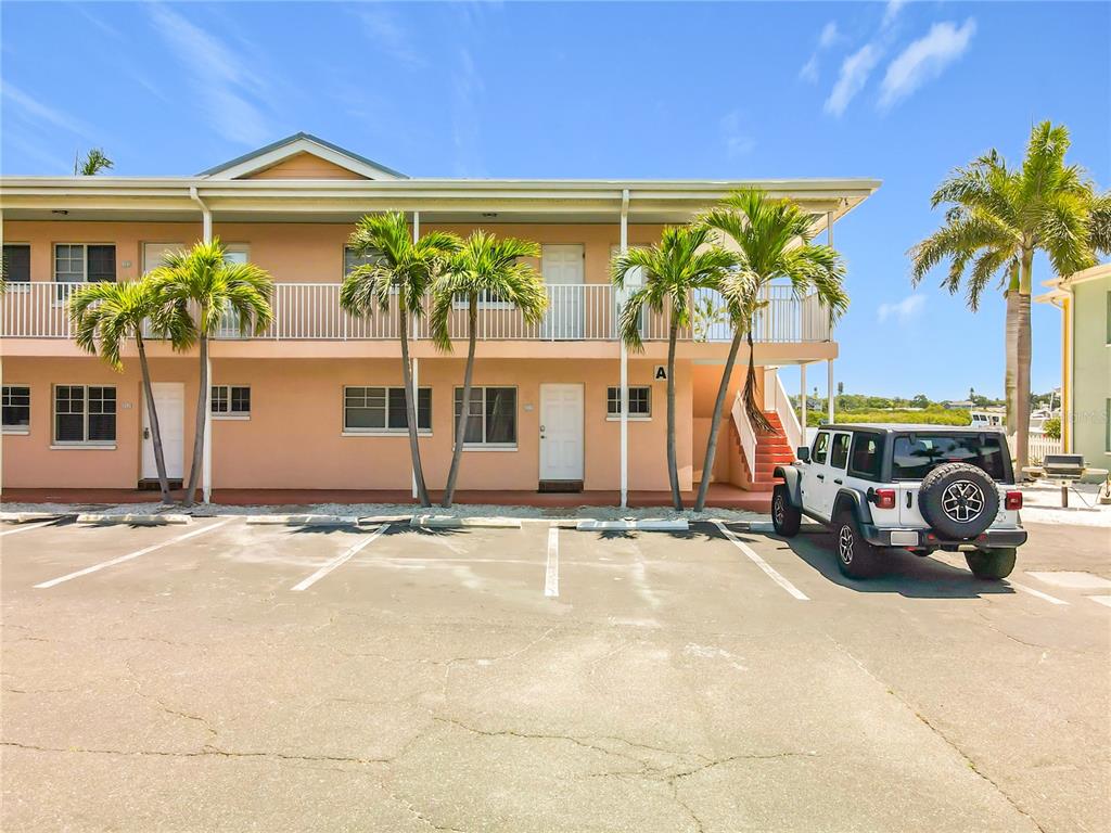 A two-story peach-colored apartment building features a parking lot and palm trees in front — 19417 GULF BOULEVARD UNIT A-113, INDIAN SHORES, FL