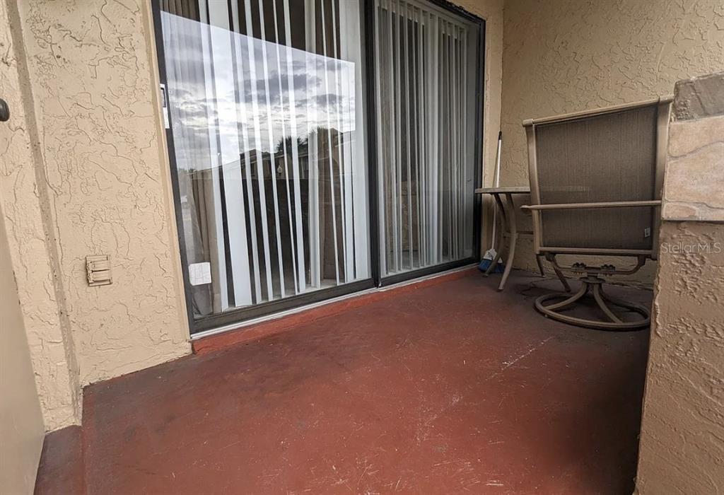 A covered patio with a red concrete floor, sliding glass doors, and a patio chair — 5229 VINELAND ROAD UNIT A106, ORLANDO, FL
