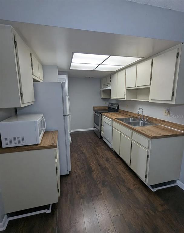 A kitchen features light-colored cabinets, wood-look countertops, stainless steel appliances, and dark wood flooring — 5229 VINELAND ROAD UNIT A106, ORLANDO, FL