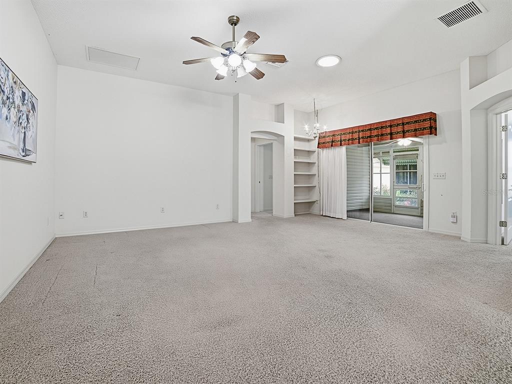 A spacious room features beige carpeting, white walls, a ceiling fan, and sliding glass doors — 16865 SE 93RD CUTHBERT CIRCLE, THE VILLAGES, FL