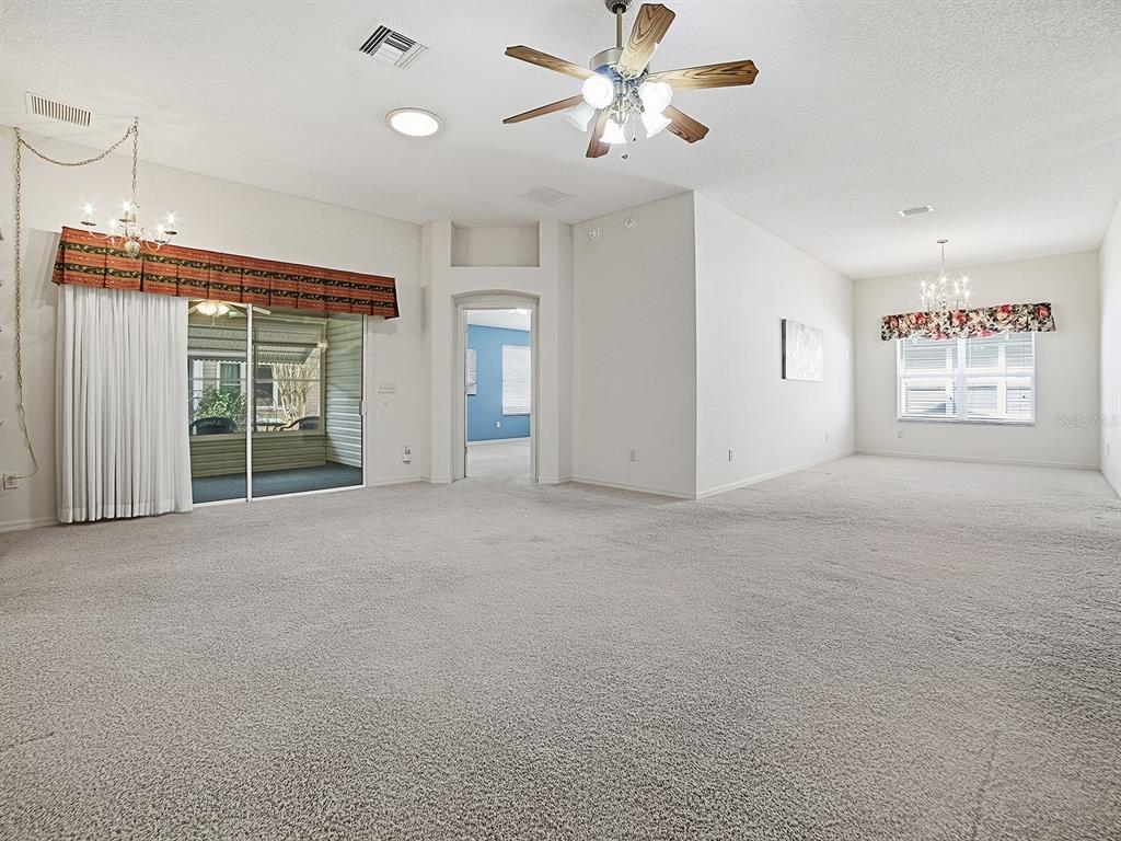 A spacious, carpeted living room features a ceiling fan, sliding glass doors, and a chandelier — 16865 SE 93RD CUTHBERT CIRCLE, THE VILLAGES, FL