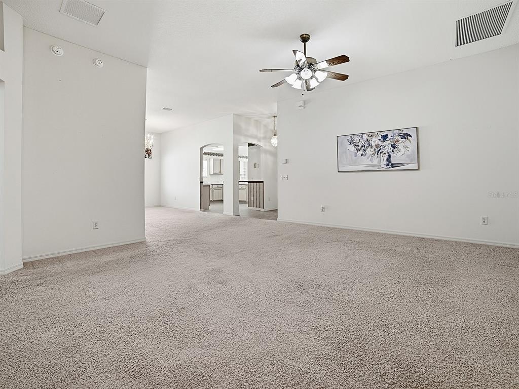 A spacious, carpeted living room features a ceiling fan and a wall-mounted floral painting — 16865 SE 93RD CUTHBERT CIRCLE, THE VILLAGES, FL