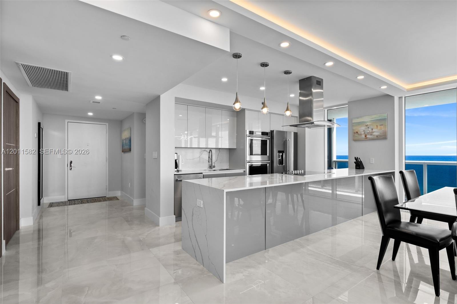 A modern kitchen features a large marble-topped island, glossy grey cabinetry, and ocean views — 1830 S Ocean Dr # 1002, Hallandale Beach FL 33009, HALLANDALE BEACH, FL