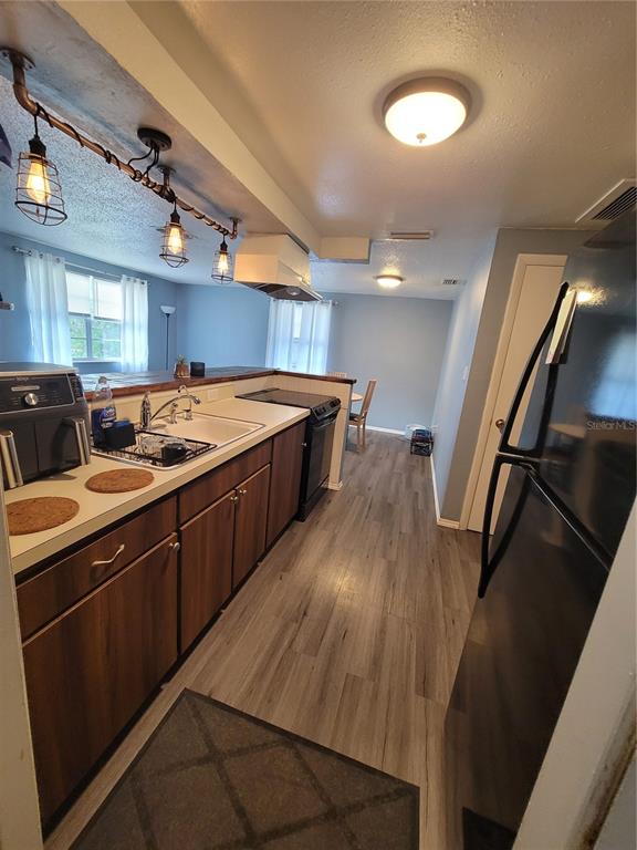 A galley-style kitchen features wood-look cabinets, black appliances, and a rustic pipe-style pendant light fixture — 10061 61ST WAY N, PINELLAS PARK, FL