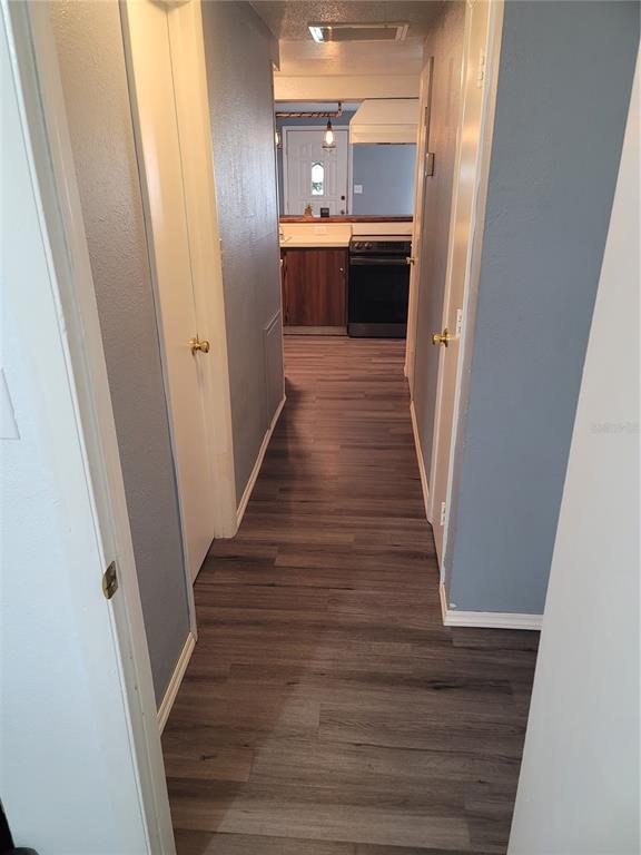 A hallway with wood-look flooring leads to a kitchen with dark cabinets and a stove — 10061 61ST WAY N, PINELLAS PARK, FL
