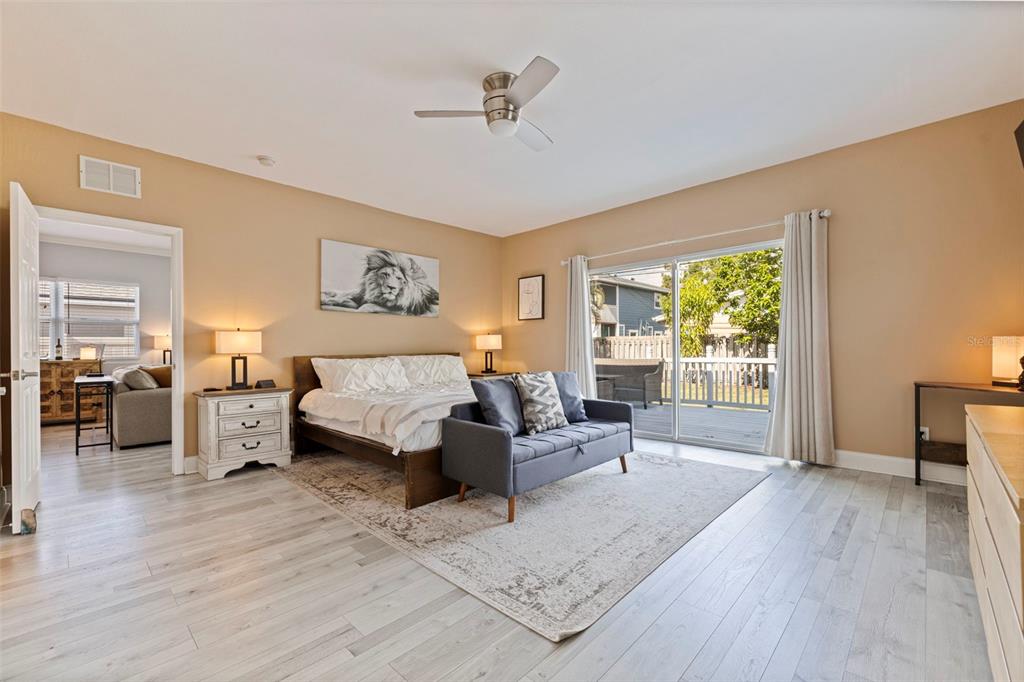 A bedroom features light wood-look flooring, a bed, a gray sofa, and a sliding glass door — 3110 15TH STREET N, ST PETERSBURG, FL