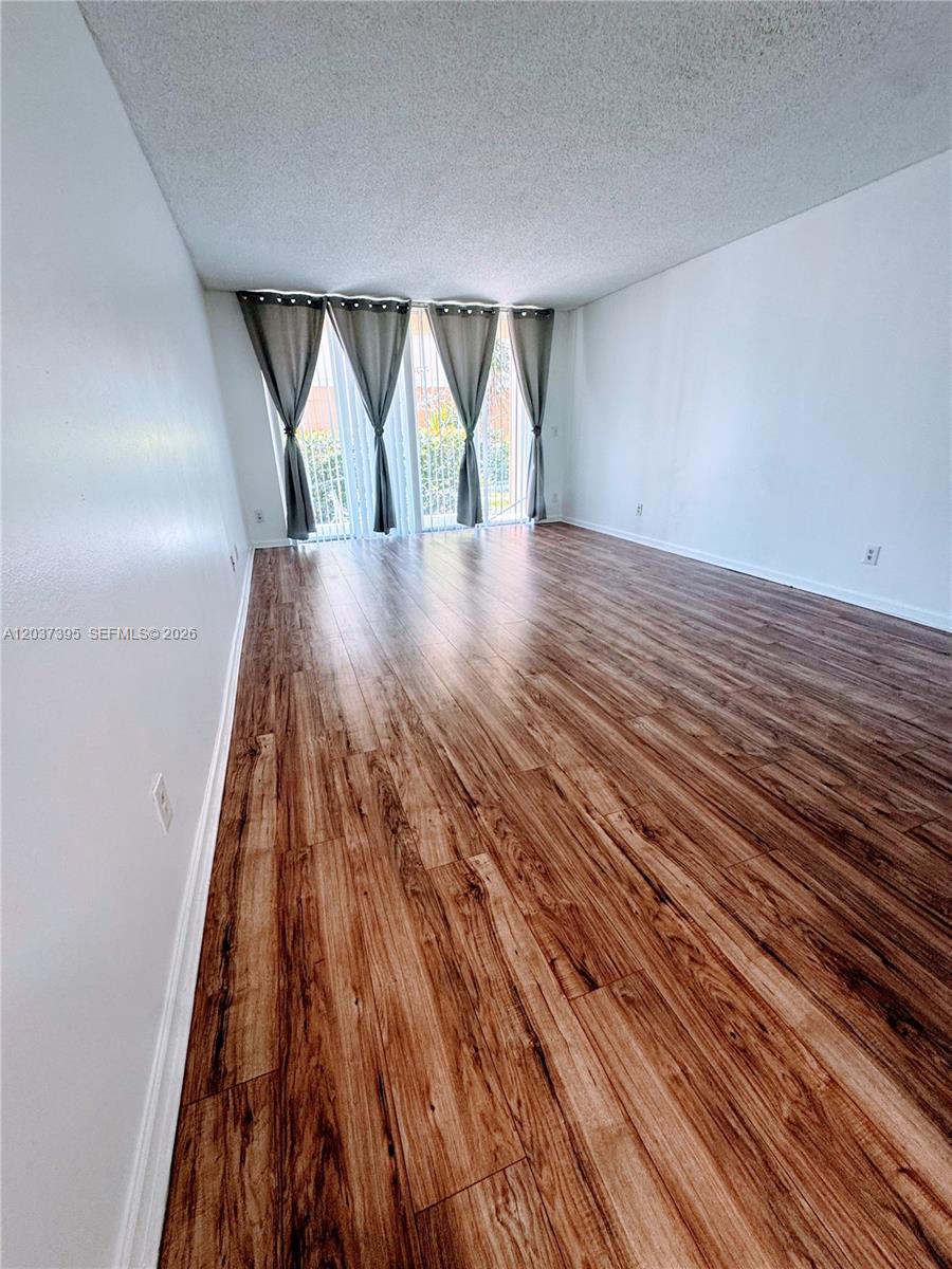An empty living area features light wood-look flooring and white walls with a kitchen pass-through — 1341 SE 3rd Ave # 112, Dania Beach FL 33004, DANIA BEACH, FL