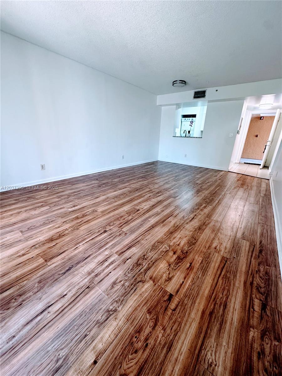 An empty living room features wood-look flooring, white walls, and a sliding glass door — 1341 SE 3rd Ave # 112, Dania Beach FL 33004, DANIA BEACH, FL