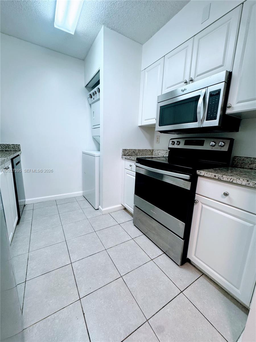 A kitchen with stainless steel appliances and tile flooring opens into a wood-floored living area — 1341 SE 3rd Ave # 112, Dania Beach FL 33004, DANIA BEACH, FL