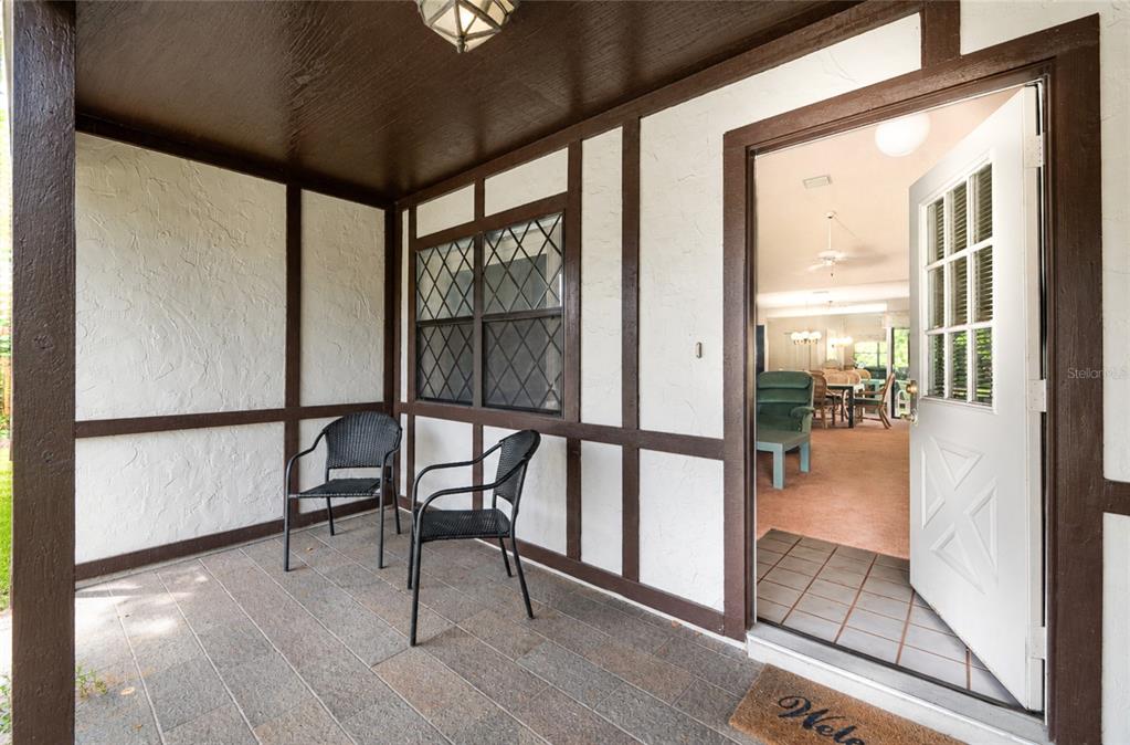 A covered porch with two chairs leads into a home through an open white door — 21 WEDGEWOOD LANE, PALM COAST, FL