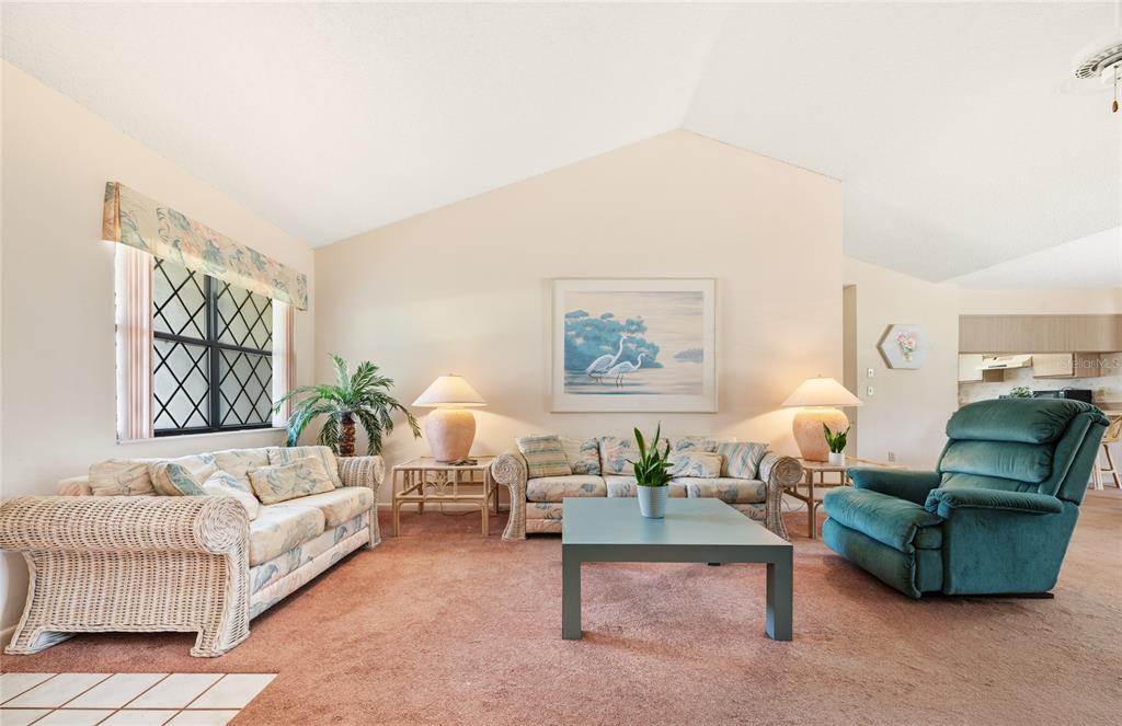 A living room features vaulted ceilings, beige carpet, two floral sofas, and a teal recliner — 21 WEDGEWOOD LANE, PALM COAST, FL