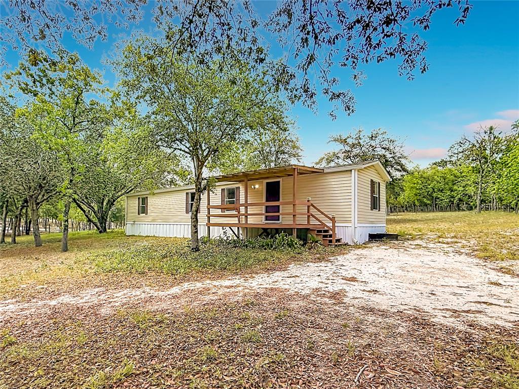 A single-story mobile home with a wooden porch sits on a wooded, sandy lot — 14671 SE 25TH STREET, MORRISTON, FL