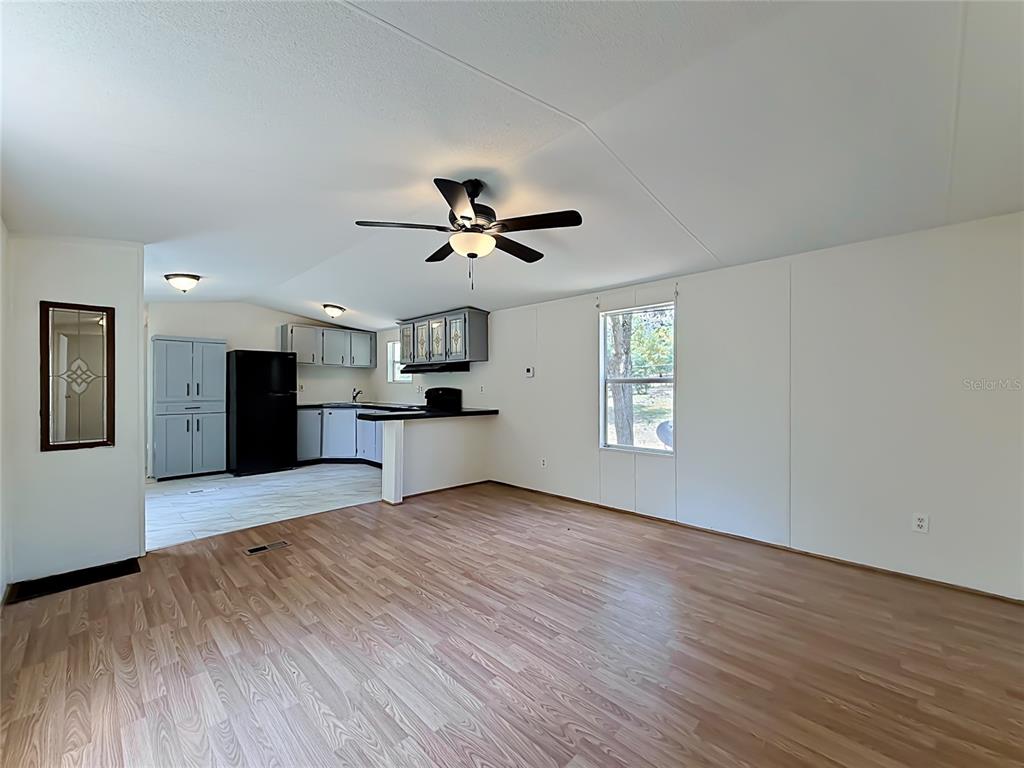 An open-concept living room with wood-look flooring leads into a kitchen with grey cabinets — 14671 SE 25TH STREET, MORRISTON, FL