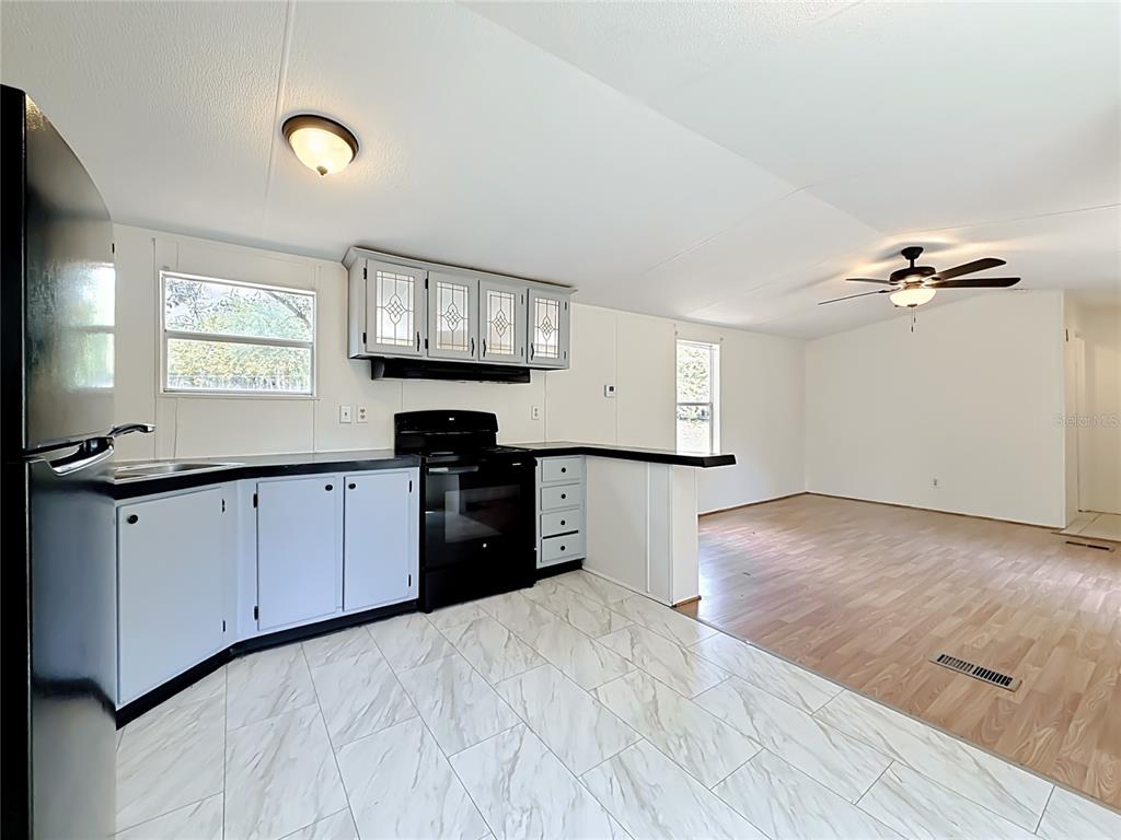 A kitchen with gray cabinets, black appliances, and white marble-look tile floors opens to a living area — 14671 SE 25TH STREET, MORRISTON, FL
