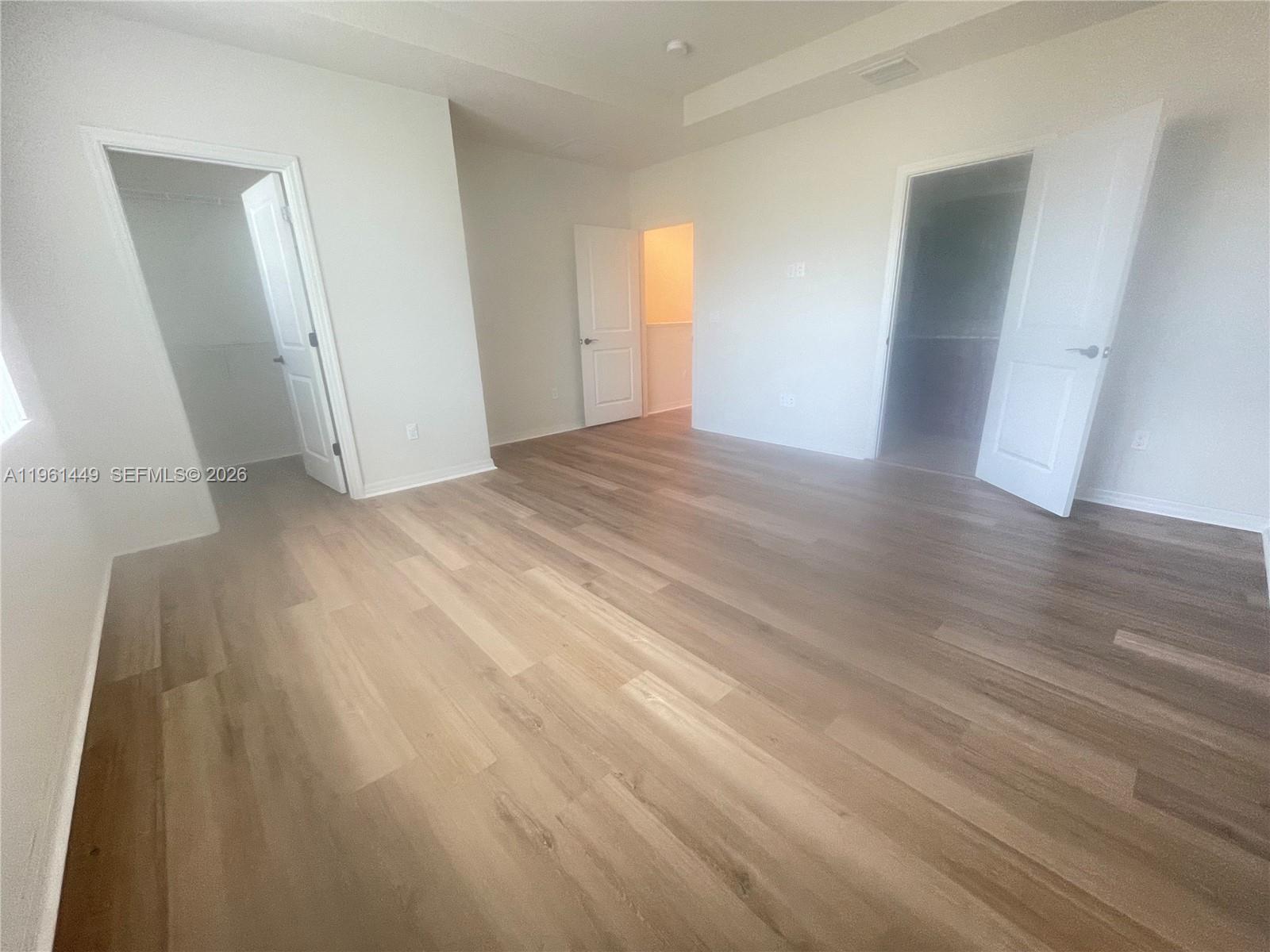 An empty bedroom features light wood-look flooring, white walls, and three open doorways — 5060 Eucalyptus Dr # 2, Hollywood FL 33021, HOLLYWOOD, FL