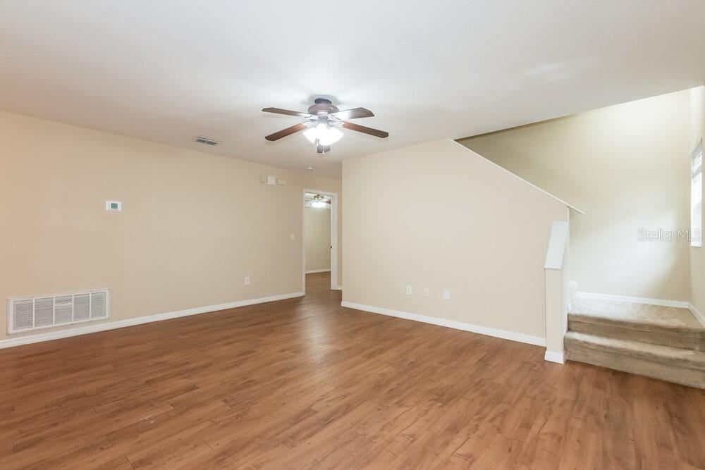 An empty living room features light-colored walls, wood-look flooring, a ceiling fan, and carpeted stairs — 6221 KITERIDGE DRIVE, LITHIA, FL