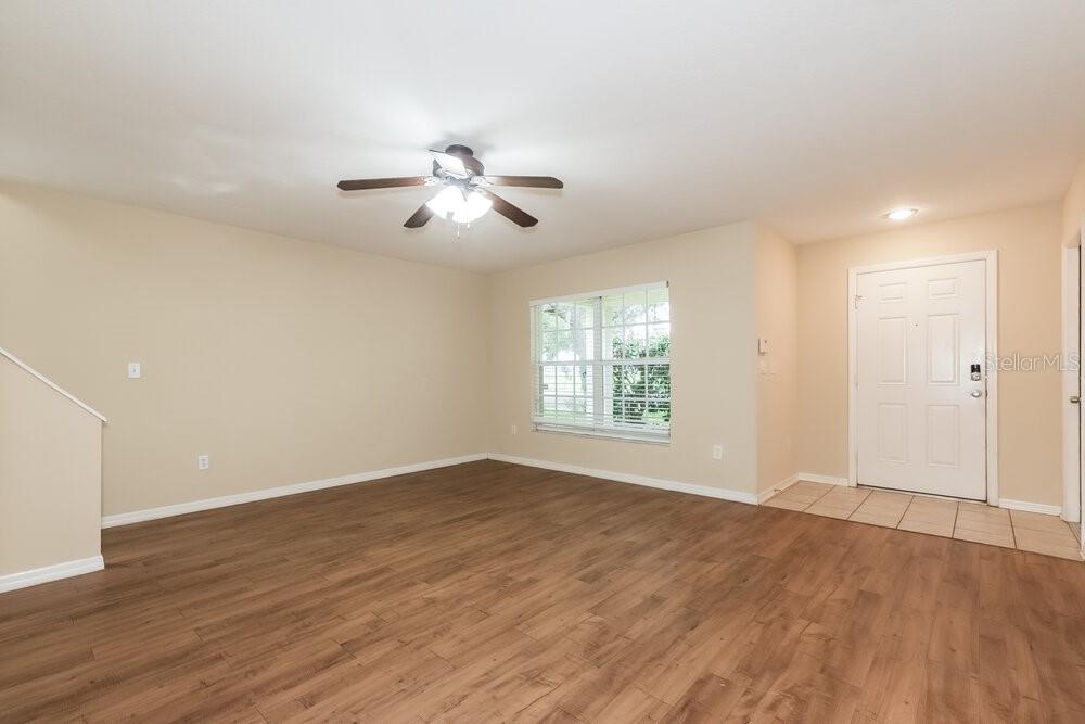 An empty living room features wood-look flooring, beige walls, a ceiling fan, and a front door — 6221 KITERIDGE DRIVE, LITHIA, FL