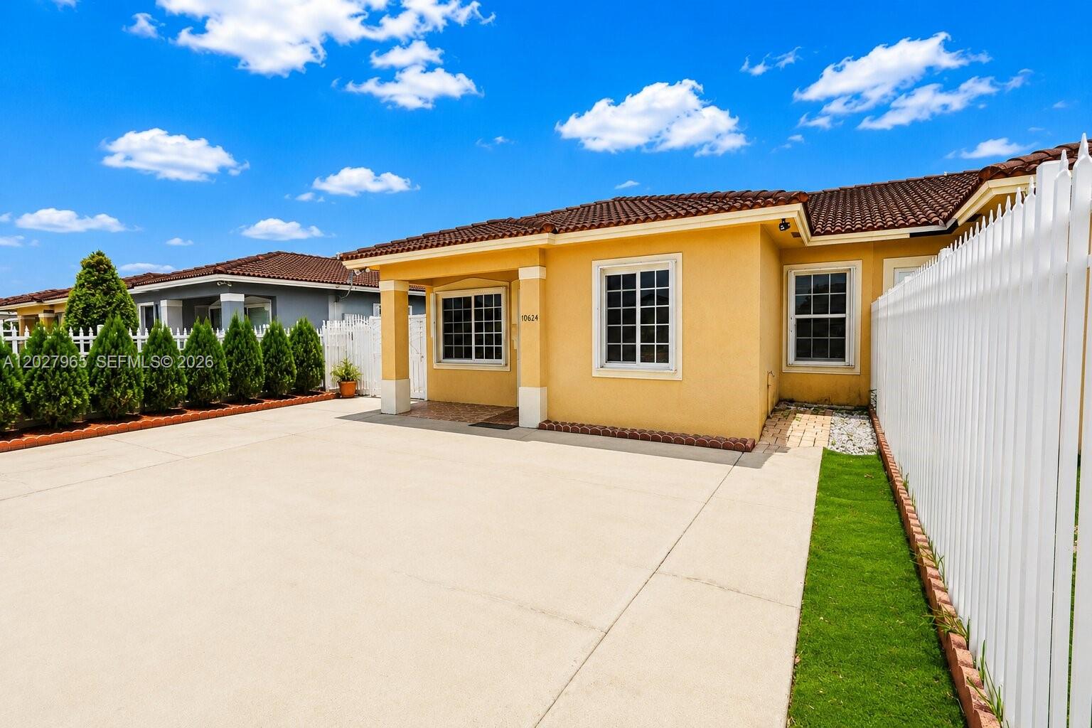 A yellow stucco house with a tiled roof and a concrete driveway under a sky — 10624 SW 181st St, Miami FL 33157, MIAMI, FL