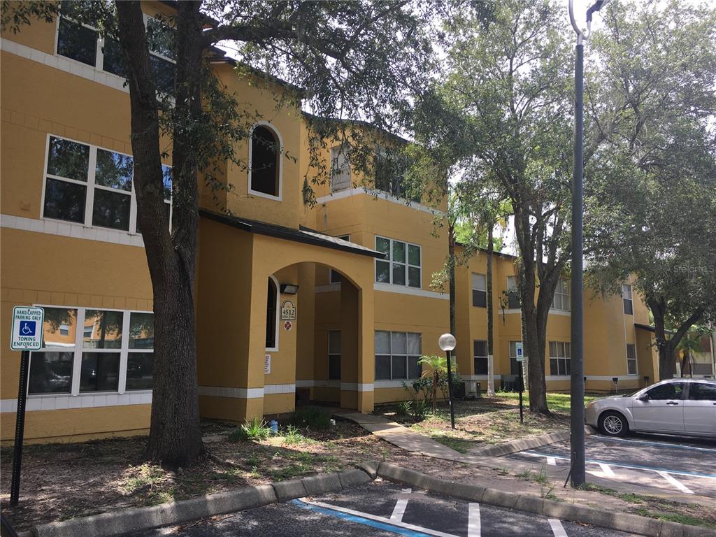A three-story yellow apartment building with a covered entrance and a parking lot — 4512 COMMANDER DRIVE UNIT 1725, ORLANDO, FL