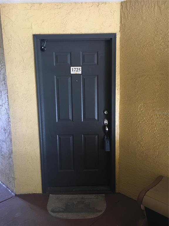 A dark gray front door with the number 1725 is set against yellow textured walls — 4512 COMMANDER DRIVE UNIT 1725, ORLANDO, FL
