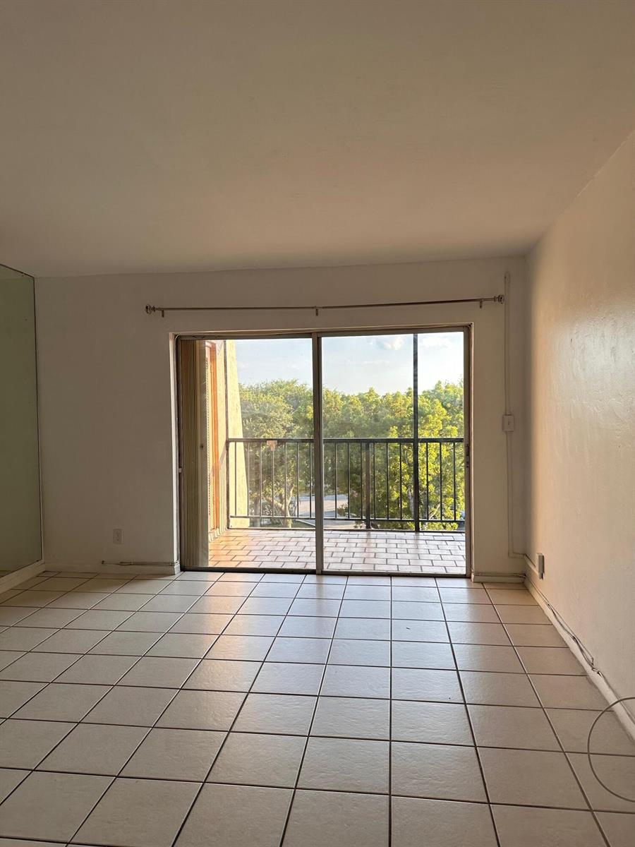 An empty room with light-colored tile flooring and a sliding glass door leading to a balcony — 13707 Kendale Lakes Circle, Miami FL 33183, MIAMI, FL