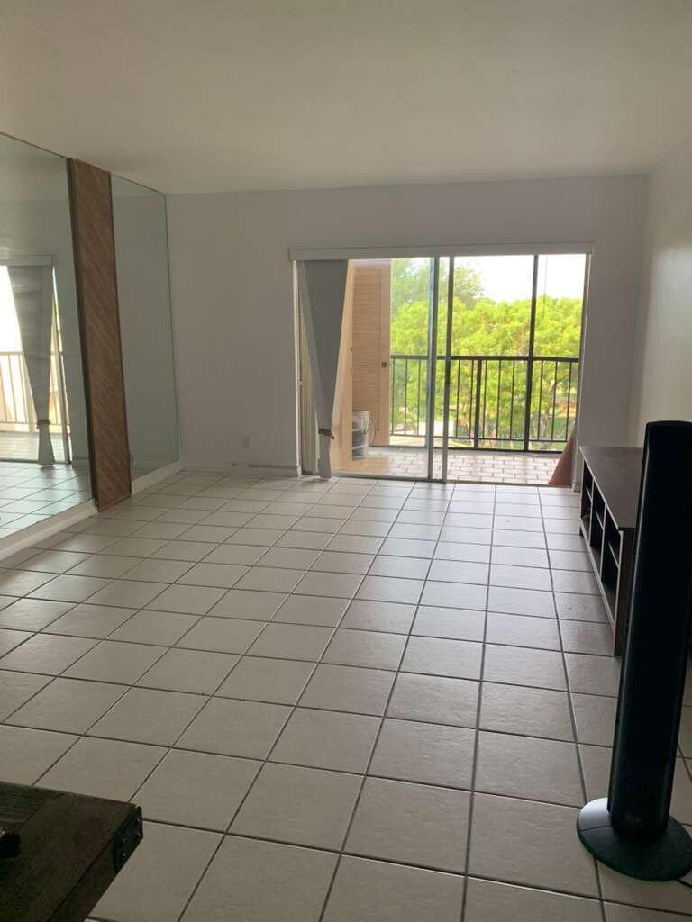 An empty living room with tiled floors, a mirrored wall, and a sliding glass balcony door — 13707 Kendale Lakes Circle, Miami FL 33183, MIAMI, FL