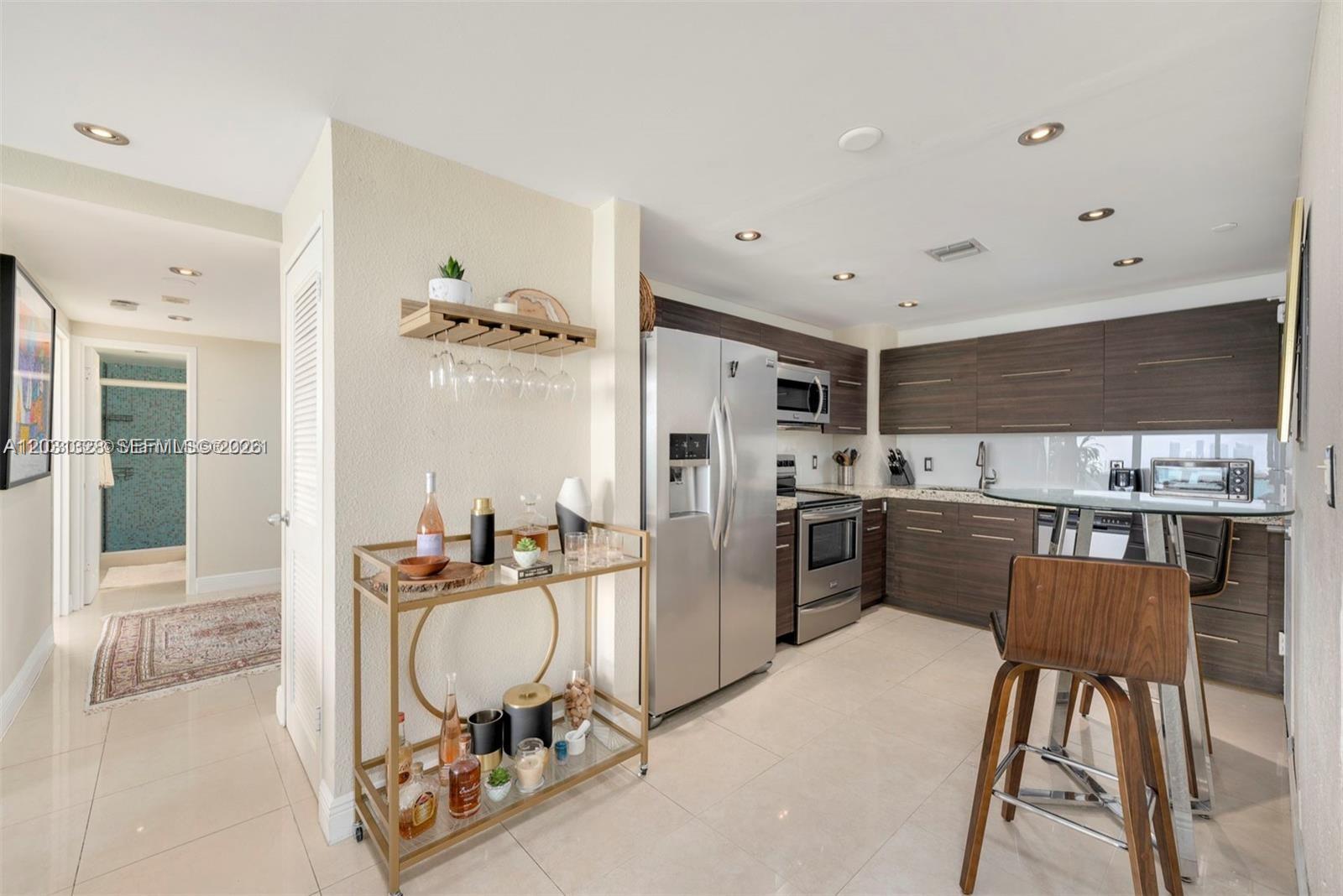A kitchen features dark wood cabinetry, stainless steel appliances, a bar cart, and tile flooring — 1200 West Ave # 725, Miami Beach FL 33139, MIAMI BEACH, FL