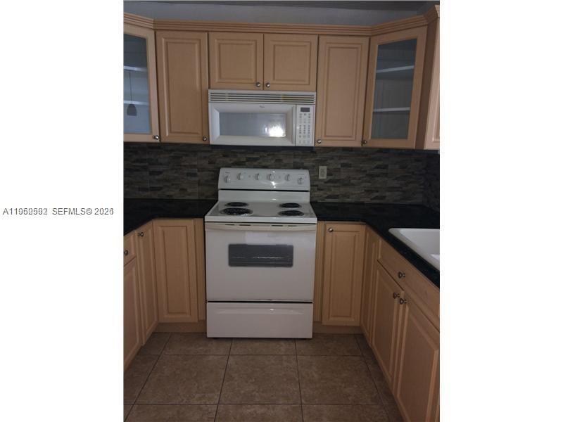 A kitchen features light wood cabinets, a white stove, a microwave, and dark countertops — 7732 Camino Real # F220, Miami FL 33143, MIAMI, FL