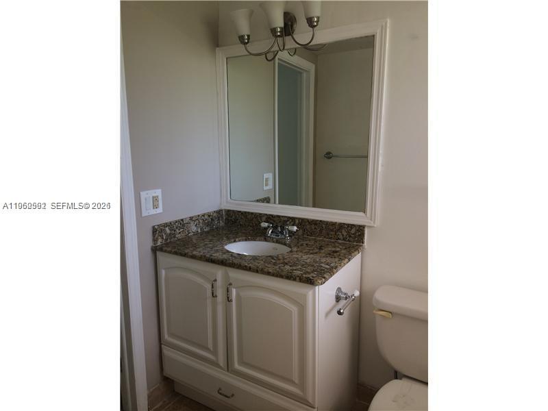 A bathroom features a white vanity with a granite countertop, a mirror, and a toilet — 7732 Camino Real # F220, Miami FL 33143, MIAMI, FL