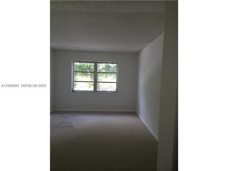 An empty room features beige carpeting, white walls, a textured ceiling, and a single window — 7732 Camino Real # F220, Miami FL 33143, MIAMI, FL